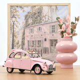 Voiture miniature Norev Citroën 2CV 1986 Paris mon amour rose poudré à l'échelle 1/18 sur fond décoratif parisien